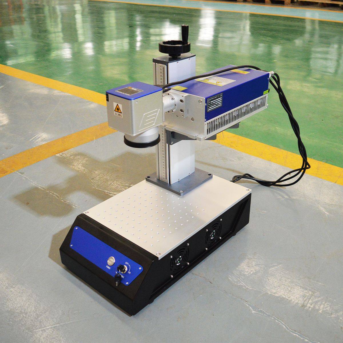 avalaser 5W UV laser engraving machine on workshop floor with visible power cables and durable metal work surface for engraving tasks.